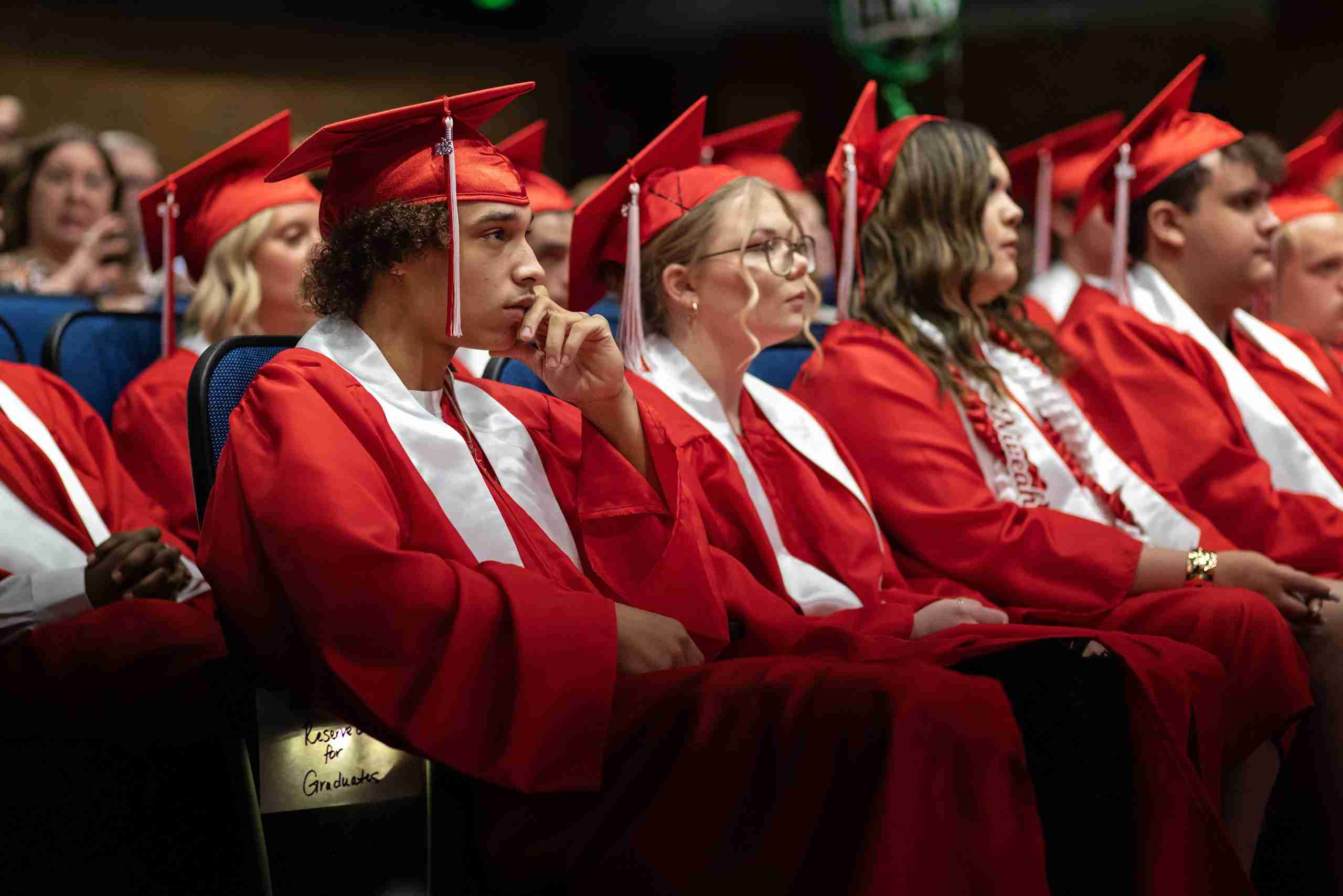 High school graduates in red caps and gowns seated during commencement ceremony.