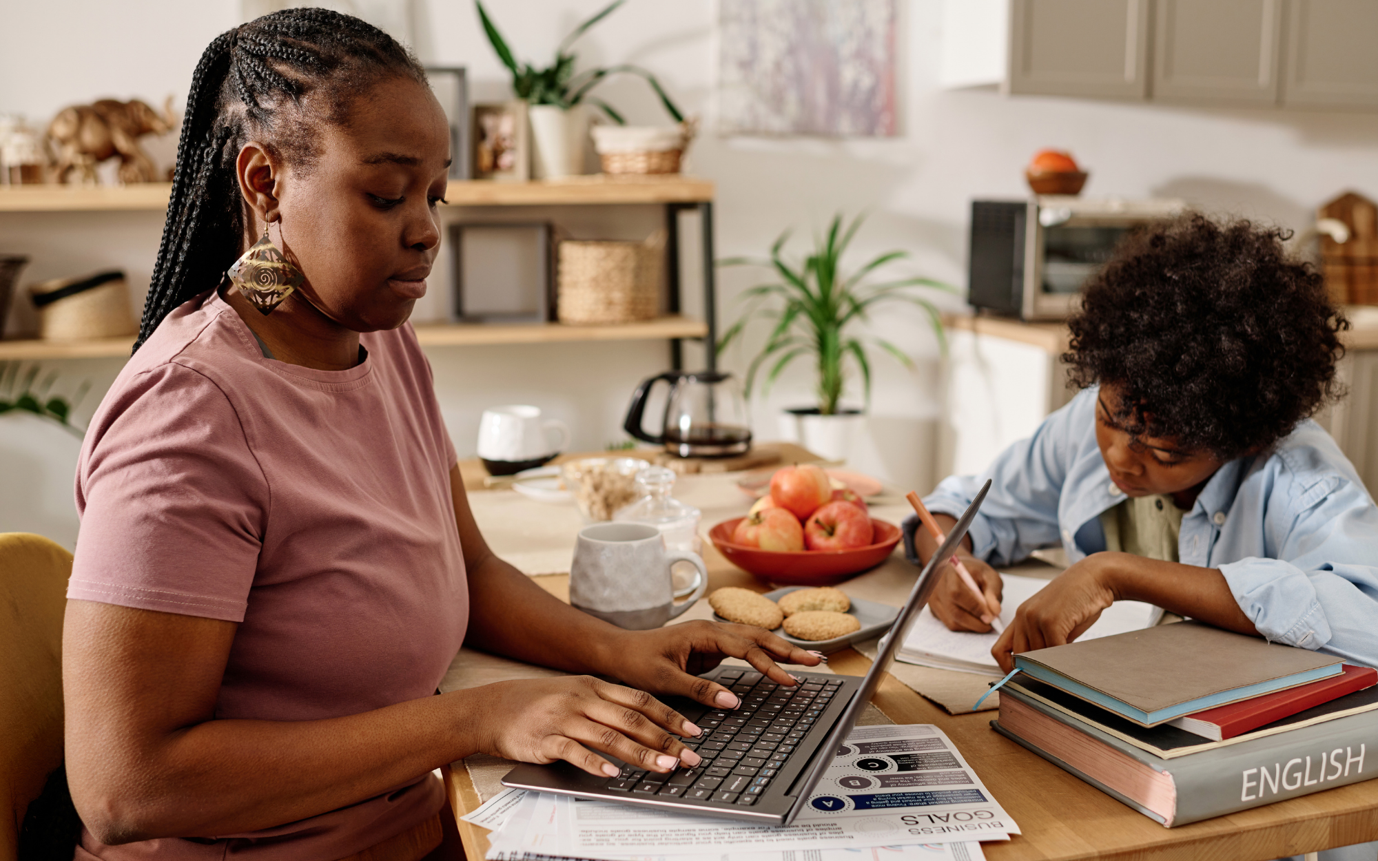 Parent working from home while supporting child with online school assignments at kitchen table, Falcon View Online Minnesota flexible learning.