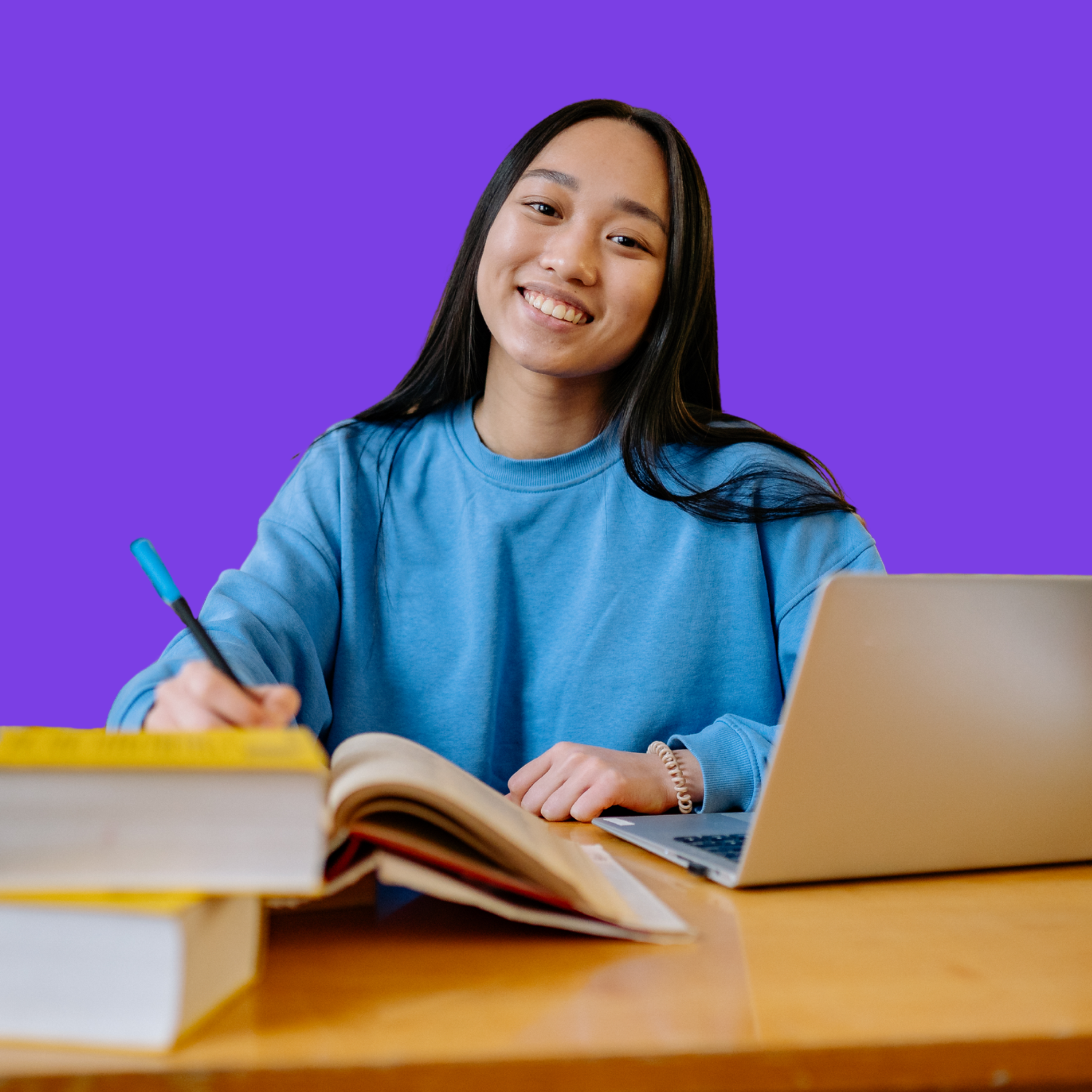 Student completing online schoolwork on a laptop with books and learning materials